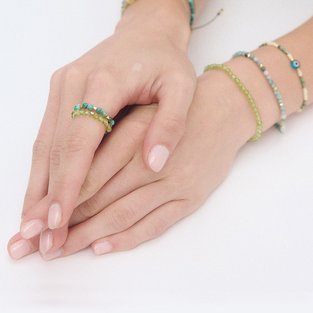 Close-up of hands wearing beaded bracelets and gemstone rings on a white background